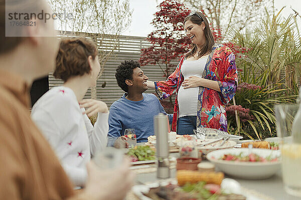 Glückliches schwangeres Paar genießt das Mittagessen mit Freunden am Terrassentisch