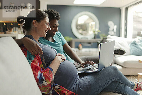Ein schwangeres Paar benutzt einen Laptop auf dem Wohnzimmersofa