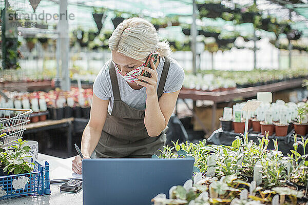 Weiblicher Gartenladenbesitzer mit Gesichtsmaske  der mit einem Smartphone telefoniert