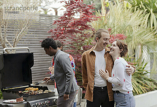 Glückliches junges Paar beim Grillen auf der Terrasse mit Freunden