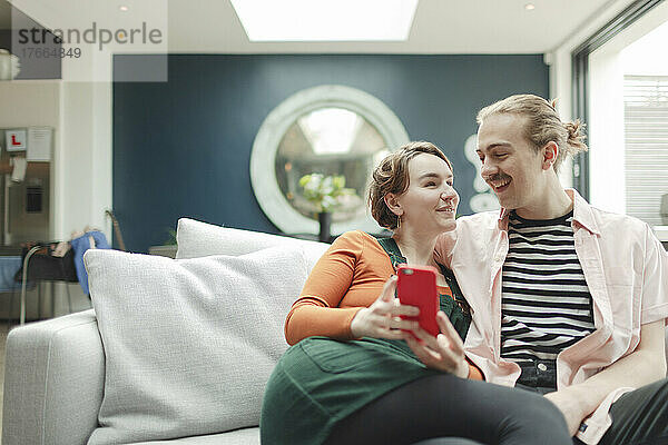 Glückliches Paar mit Smartphone auf dem Wohnzimmersofa