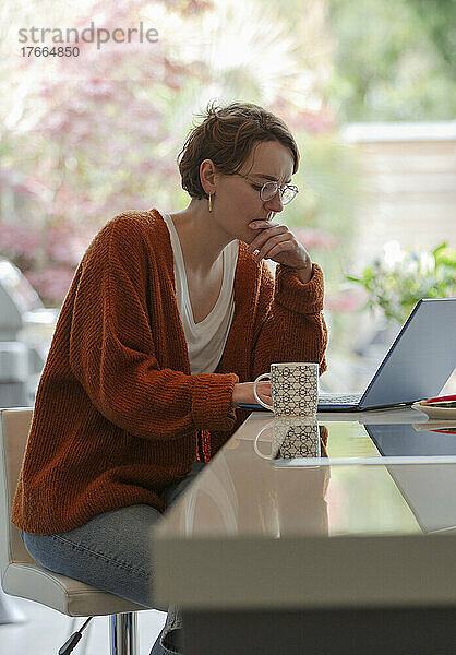 Konzentrierte junge Frau arbeitet von zu Hause aus am Laptop