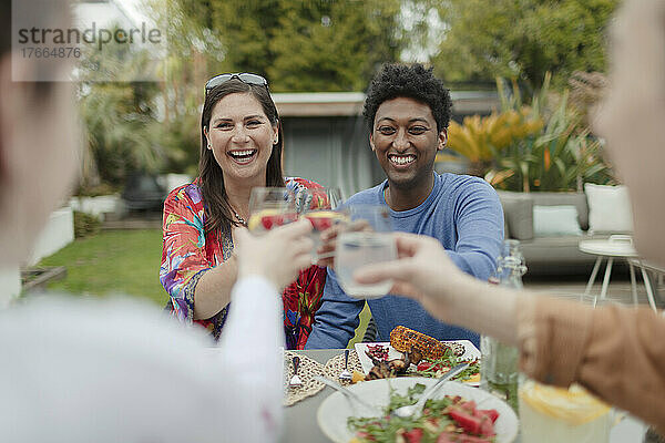 Fröhliche Freunde stoßen mit Gläsern am Terrassentisch auf das Mittagessen an