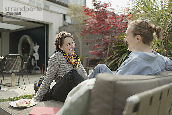 Glückliches junges Paar unterhält sich auf einem sonnigen Liegestuhl auf der Terrasse