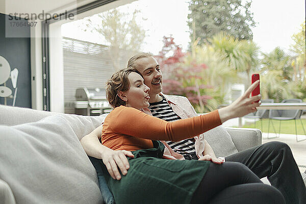 Verspieltes junges Paar macht Selfie mit Smartphone auf Sofa