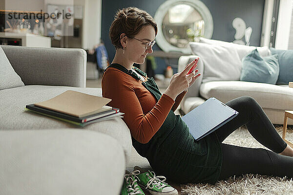 Junge Frau mit Laptop und Smartphone im Wohnzimmer