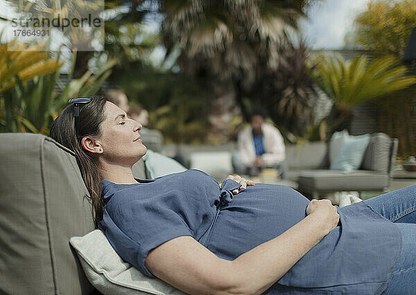 Serene schwangere Frau entspannt auf sonnigen Terrasse Liegestuhl