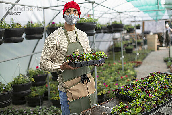 Porträt selbstbewusster männlicher Gärtnereibesitzer mit Gesichtsmaske und Pflanzen
