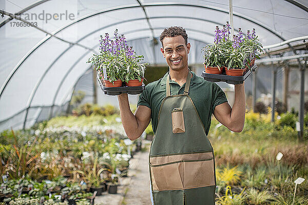 Porträt lächelnder männlicher Gärtnereiarbeiter mit Blumen im Gewächshaus