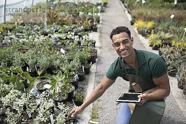 Porträt glücklicher männlicher Gartenladenbesitzer mit digitalem Tablet und Pflanzen