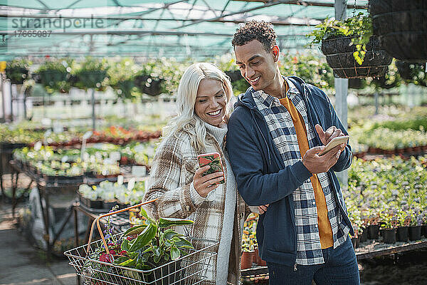 Ehepaar mit Smartphones beim Einkaufen im Gartengeschäft
