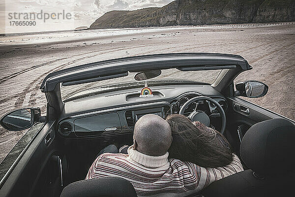 Zärtliches Paar  das sich im Cabrio am Winterstrand umarmt