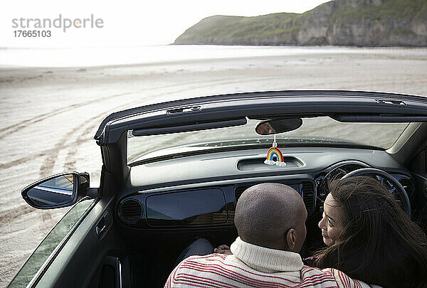 Zärtliches Paar umarmt sich im Cabrio am Strand
