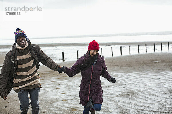 Glückliches  sorgloses Paar  das sich an den Händen hält und am nassen Winterstrand läuft