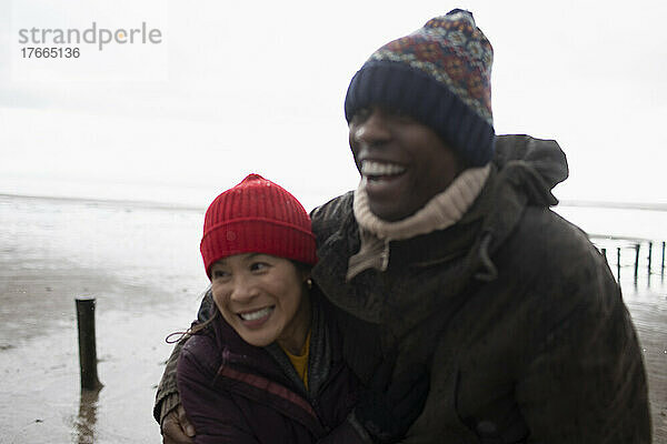 Glückliches zärtliches Paar in warmer Kleidung  das sich am Winterstrand umarmt