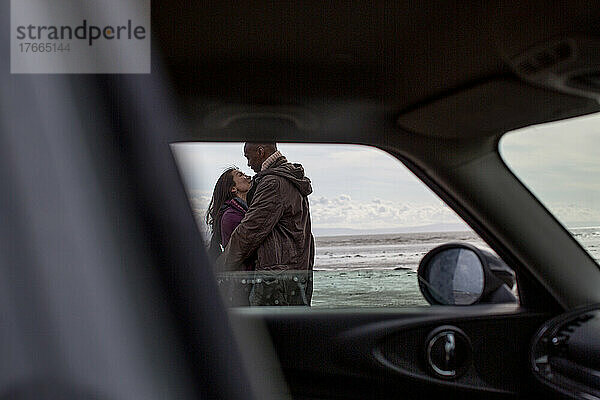Zärtliches Paar  das sich außerhalb des Autos am Strand umarmt