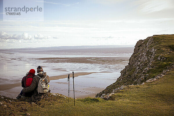 Wandererpaar  das auf einer Klippe über dem ruhigen Wintermeerstrand eine Pause einlegt