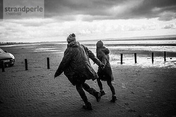 Paar hält sich an den Händen und läuft am Winterstrand