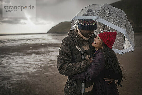 Glückliches Paar unter Regenschirm am nassen Winterstrand