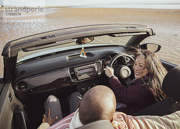 Glückliches Paar fährt Cabrio am sonnigen Strand