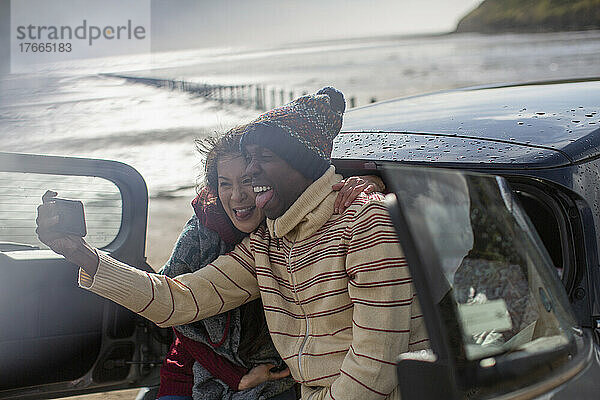 Glückliches verspieltes Paar macht Selfie im Auto am Winterstrand