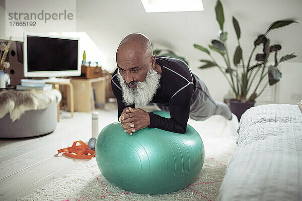 Älterer Mann mit Bart trainiert mit Fitnessball zu Hause