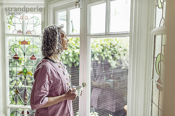 Glückliche ältere Frau mit Tee am Fenster