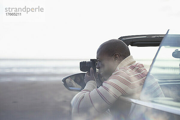 Mann mit Digitalkamera im Cabrio am Winterstrand