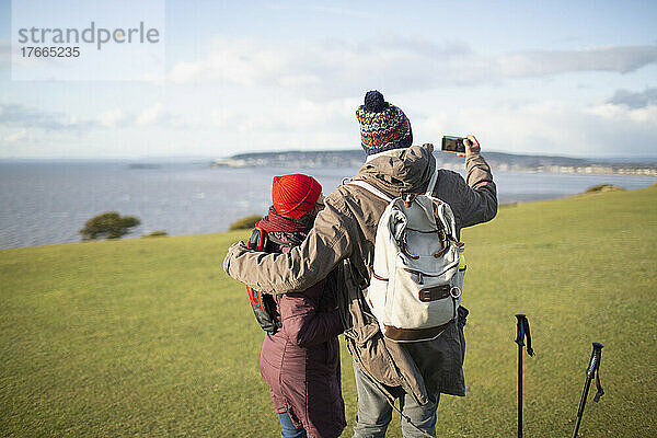 Wandererpaar mit Fotohandy auf Klippe mit sonnigem Meerblick