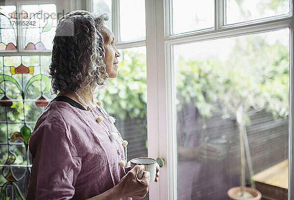 Nachdenkliche ältere Frau trinkt Tee am Fenster