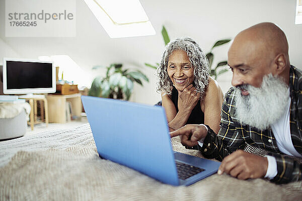 Glückliches älteres Paar mit Laptop auf dem Bett