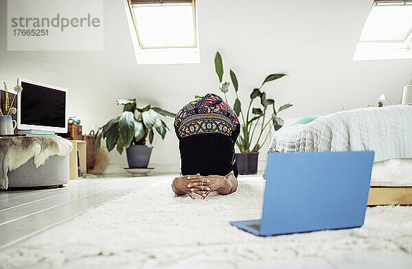 Frau übt Yoga online mit Laptop auf dem Schlafzimmerteppich