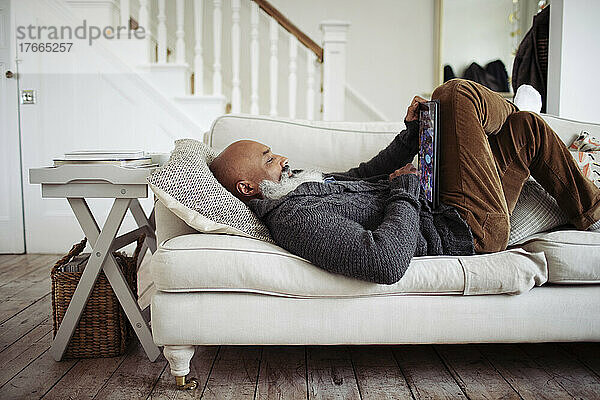 Älterer Mann entspannt sich auf dem Wohnzimmersofa mit digitalem Tablet