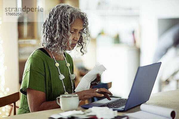 Ältere Frau mit Quittungen beim Banking am Laptop