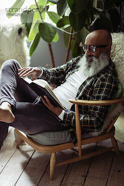 Älterer Mann mit Bart liest Buch im Sessel