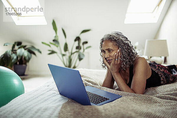 Ältere Frau mit Laptop auf dem Bett