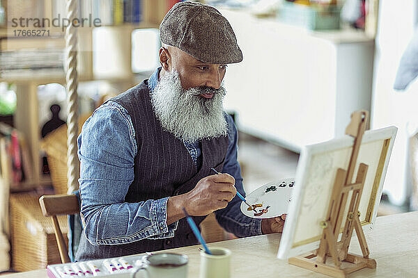 Älterer Mann mit Bart malt an Staffelei