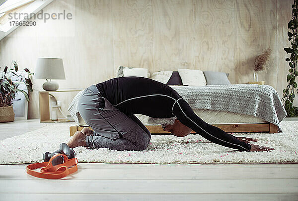 Älterer Mann übt in Yoga-Kinder-Pose auf Schlafzimmerboden