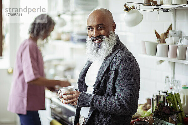 Portrait glücklicher reifer Mann mit Bart trinkt Kaffee in der Küche