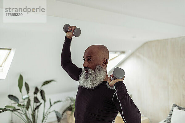 Älterer Mann mit Bart trainiert mit Hanteln zu Hause