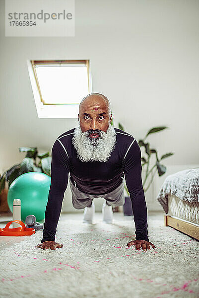 Konzentrierter reifer Mann  der in Plankenhaltung auf dem Schlafzimmerboden trainiert
