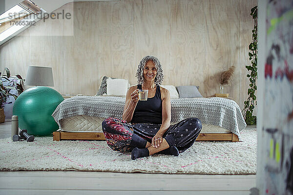 Porträt einer glücklichen älteren Frau  die auf dem Boden eines Schlafzimmers Wasser trinkt