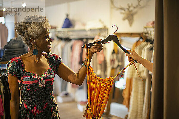 Eine Ladenbesitzerin gibt einer Kundin in einer Boutique ein Kleid auf einem Bügel