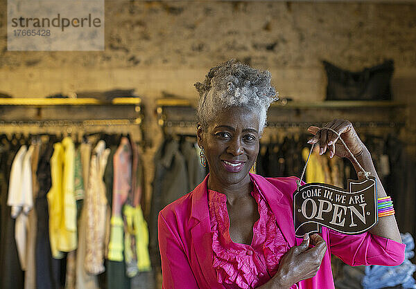 Porträt einer selbstbewussten älteren Ladenbesitzerin mit offenem Schild