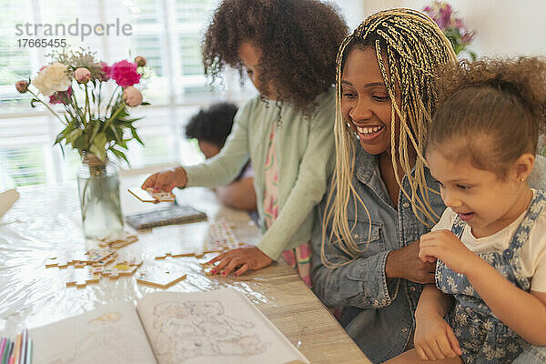 Glückliche Mutter und Töchter beim Malen und Spielen am Tisch