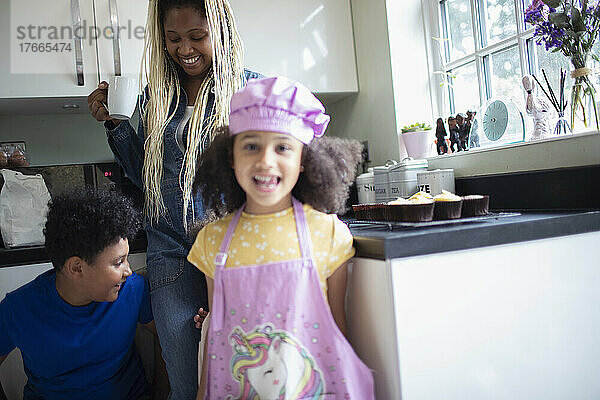 Portrait glückliches Mädchen in Einhornschürze in Küche mit Familie