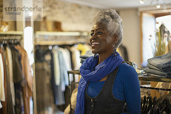 Glückliche Ladenbesitzerin mit blauem Schal in einer Bekleidungsboutique