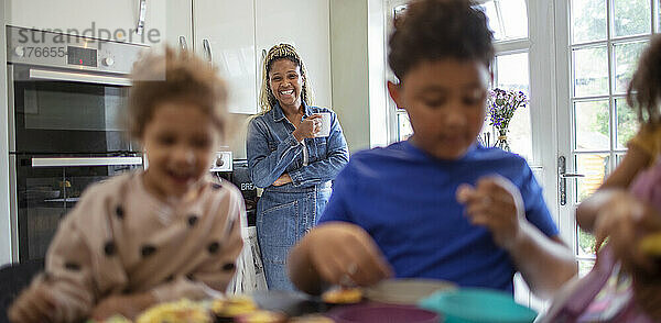 Glückliche Mutter schaut Kindern beim Backen in der Küche zu