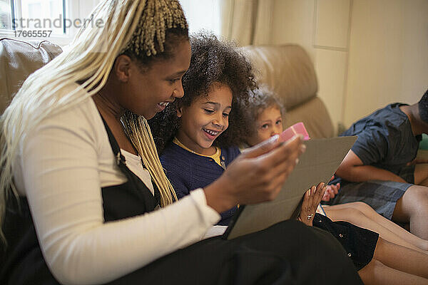 Glückliche Mutter und Tochter nutzen digitales Tablet auf dem Sofa im Wohnzimmer