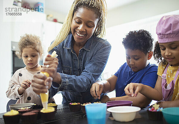 Glückliche Mutter und Kinder dekorieren Cupcakes in der Küche